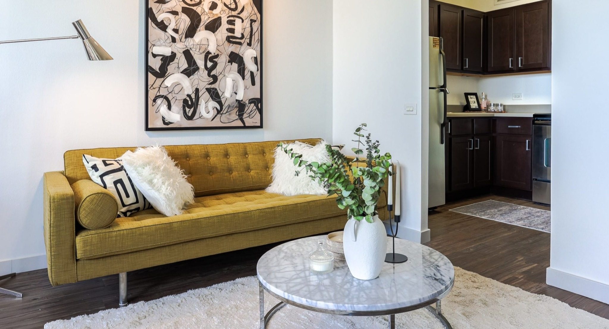 Contemporary living space at Presidential Towers in Chicago with mustard sofa, art wall, floor lamp, and open doorway to the updated kitchen