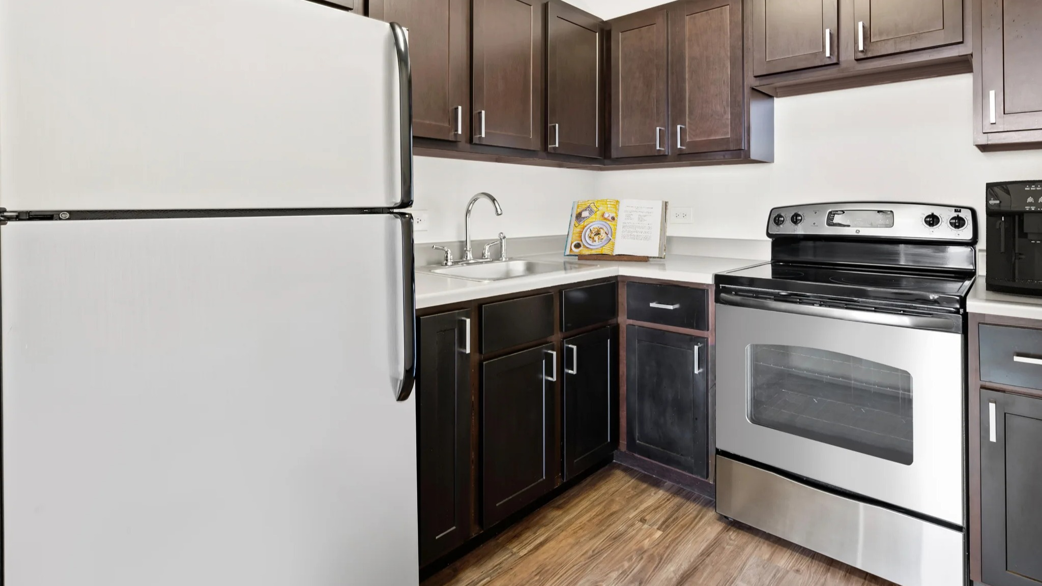 Modern resident kitchen with dark cabinetry, stainless-steel appliances, and wood-style floors at Presidential Towers in Chicago