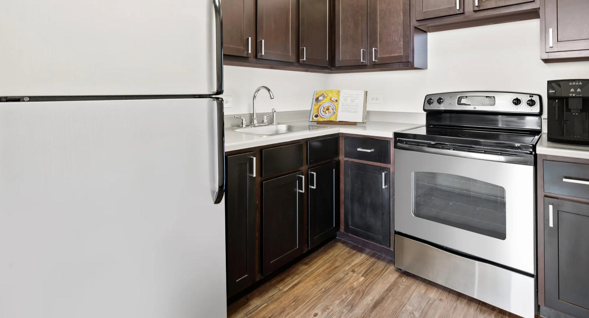 Modern resident kitchen with dark cabinetry, stainless-steel appliances, and wood-style floors at Presidential Towers in Chicago
