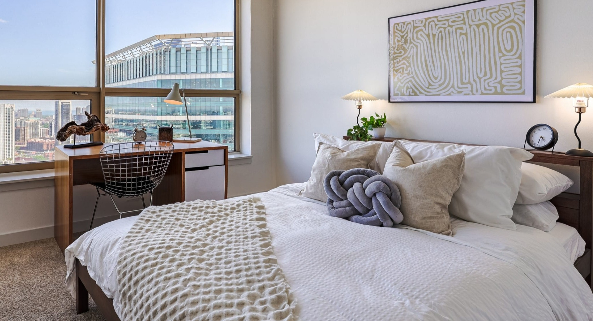 Peaceful bedroom at Presidential Towers in Chicago featuring a comfy bed, soft bedding, night lamps, and a windowed desk ideal for work with skyline views