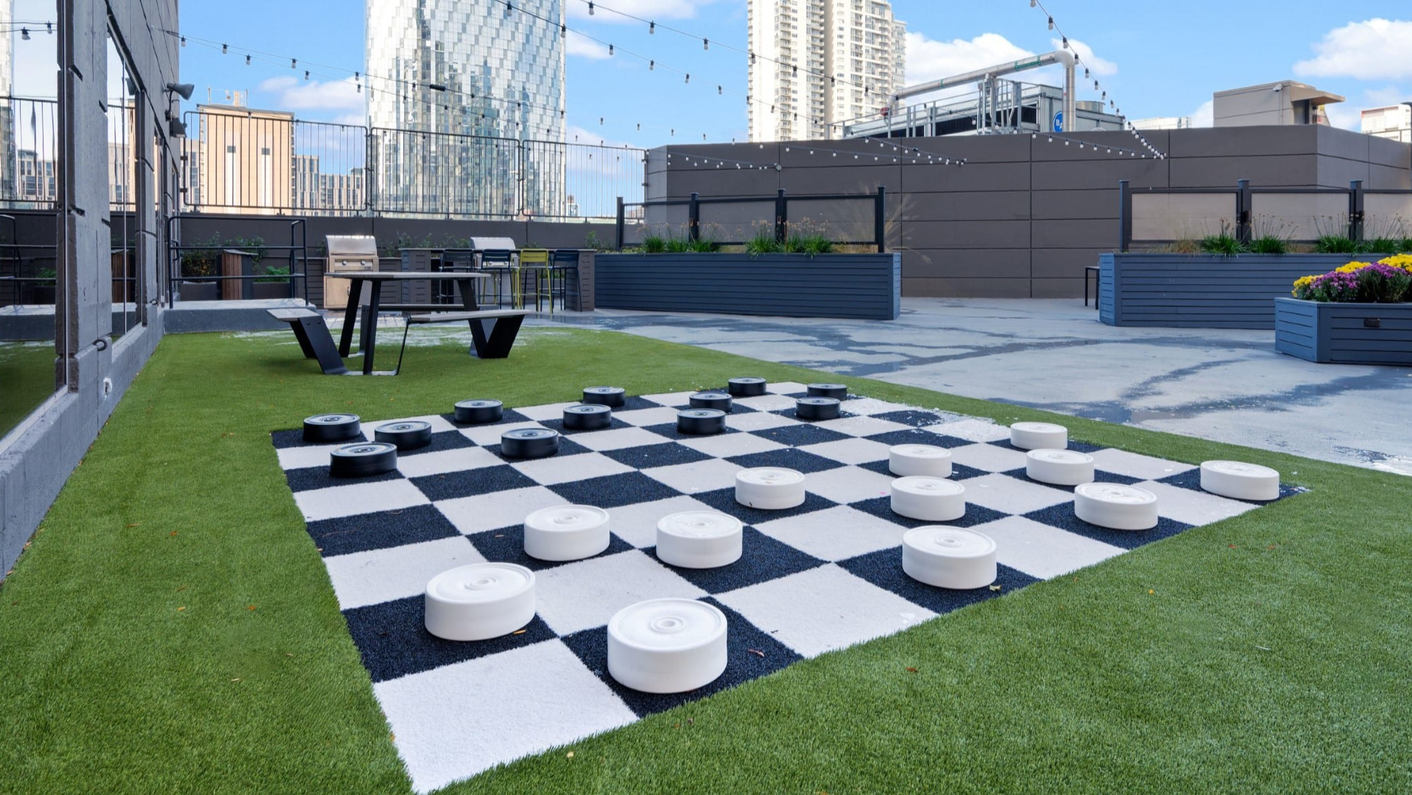 Rooftop sundeck with giant checkers, string lights, seating areas, and skyline views at Presidential Towers apartments in Chicago