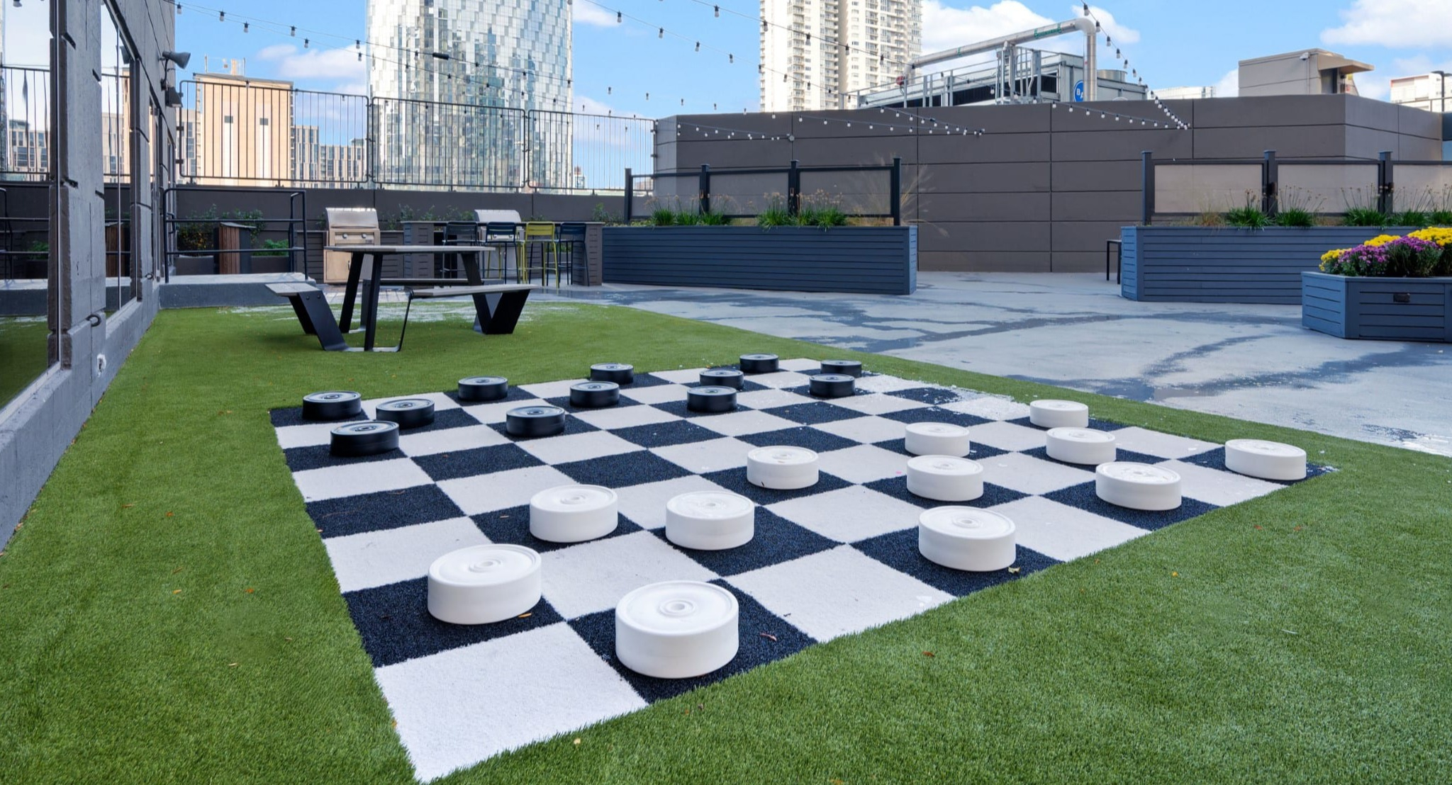 Rooftop sundeck with giant checkers, string lights, seating areas, and skyline views at Presidential Towers apartments in Chicago