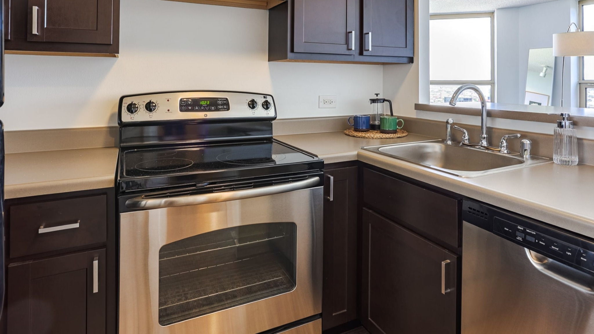 Contemporary kitchen at Presidential Towers in Chicago with stainless appliances, dark shaker cabinets, ample counter space, and a pass-through to living area
