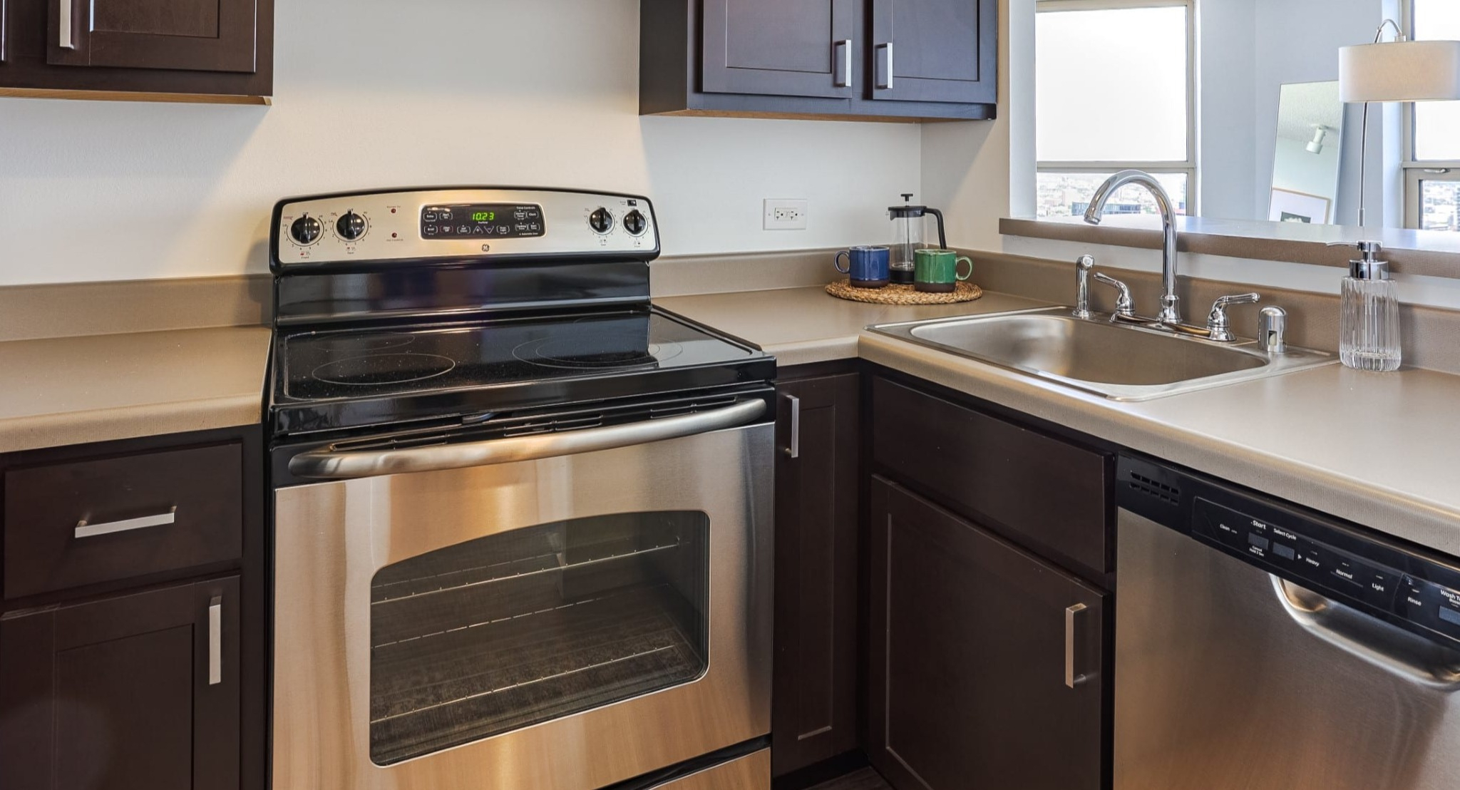 Contemporary kitchen at Presidential Towers in Chicago with stainless appliances, dark shaker cabinets, ample counter space, and a pass-through to living area