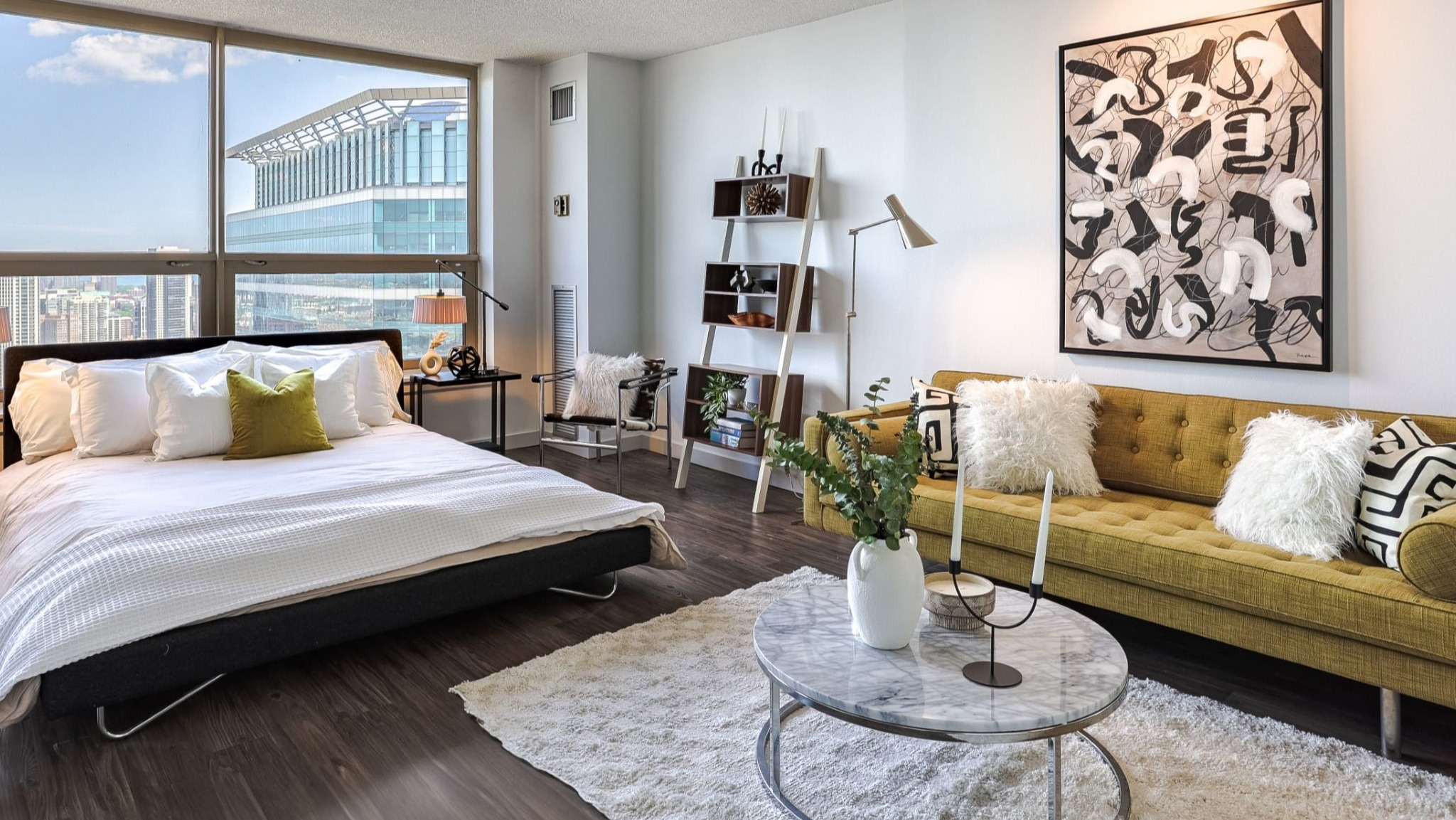 Stylish studio bedroom at Presidential Towers in Chicago with platform bed, side tables, mustard sofa, art, and wide windows bringing in natural light