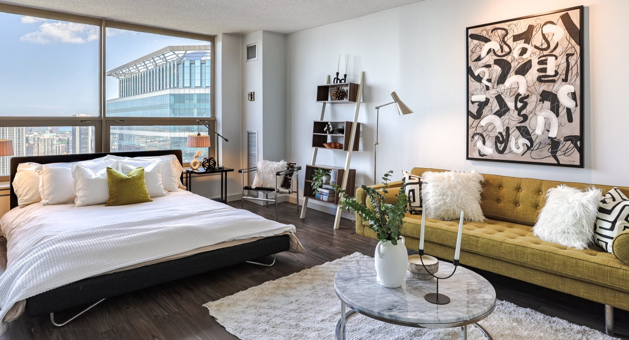 Stylish studio bedroom at Presidential Towers in Chicago with platform bed, side tables, mustard sofa, art, and wide windows bringing in natural light