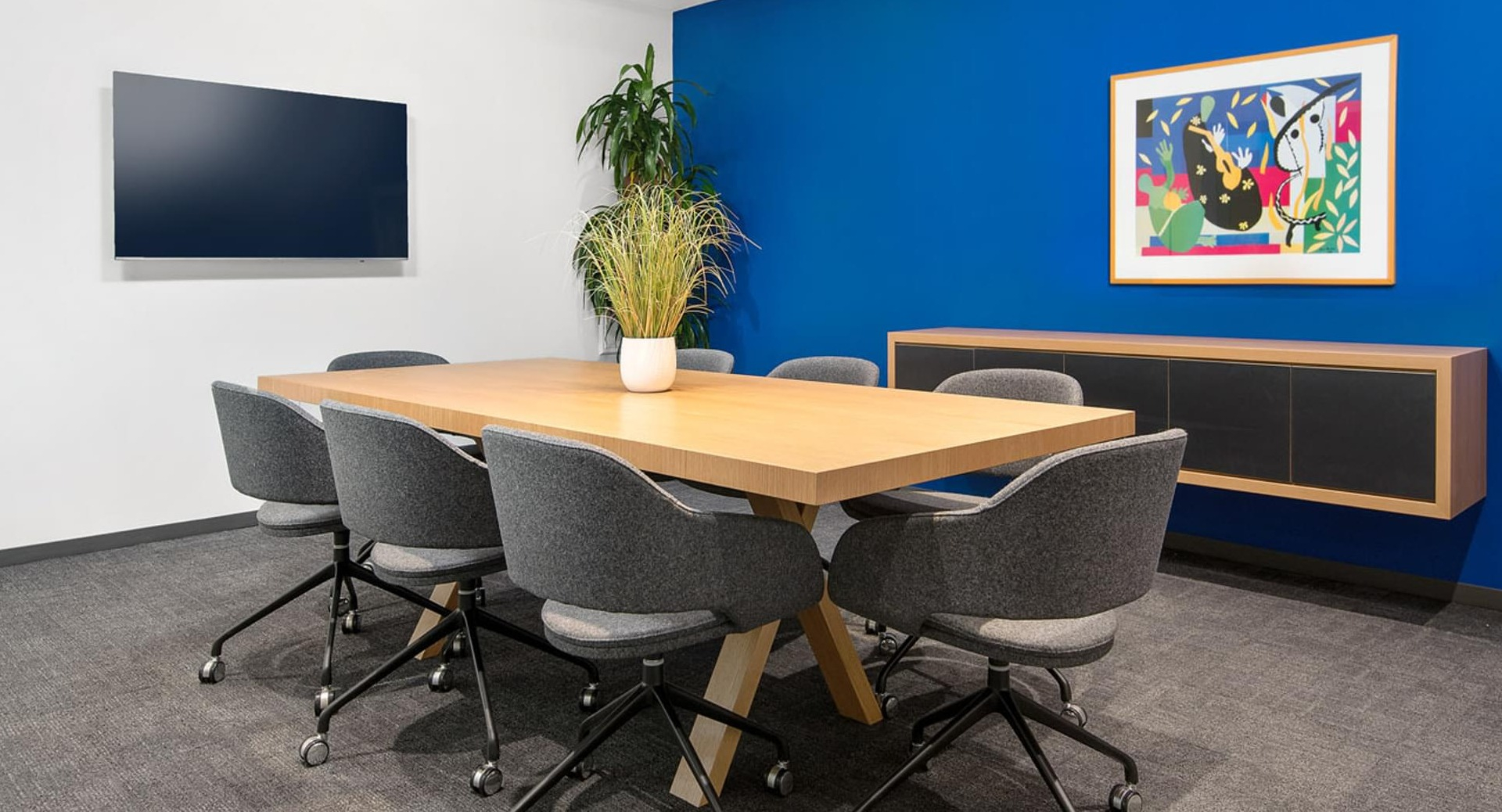 Private conference room with blue accent wall, wood table, rolling chairs, and wall display at Optima Signature apartments in Chicago