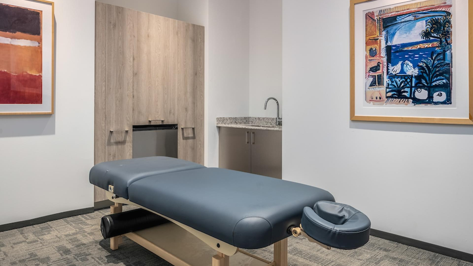 Private massage therapy room with cushioned table, modern artwork, and wood cabinetry at Optima Signature apartments in Chicago