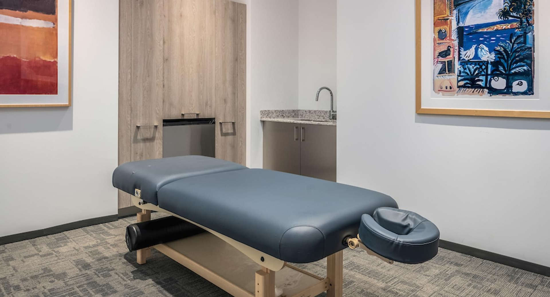 Private massage therapy room with cushioned table, modern artwork, and wood cabinetry at Optima Signature apartments in Chicago