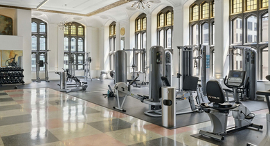 Grand fitness center at Randolph Tower City Apartments in Chicago, featuring various cardio and strength equipment, and ornate windows