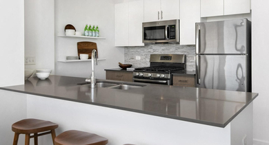 Modern apartment kitchen at Reside on Green Street in Chicago, featuring stainless steel appliances, white cabinetry, and a breakfast bar with stools