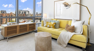 Bright apartment living room at Reside on Green Street in Chicago, featuring a vibrant yellow sofa and expansive city views through large windows