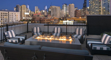 Beautiful rooftop lounge at dusk with a lit fire pit, comfortable seating, and a stunning view of the Chicago skyline at Reside on Green Street in Chicago