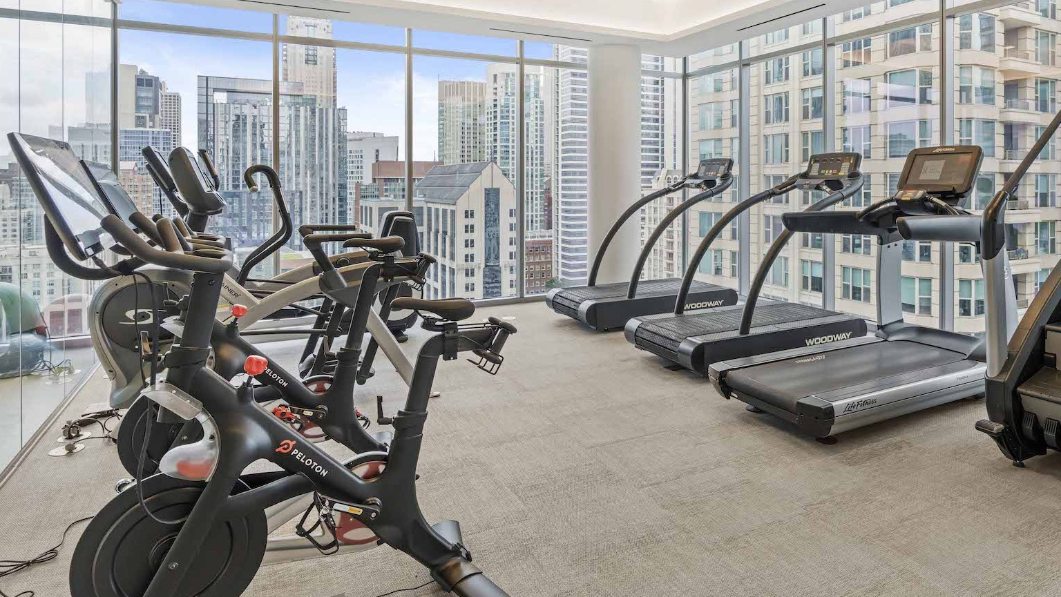 Modern cardio room with treadmills and exercise bikes, featuring large windows with city skyline views at Residences at 8 East Huron in Chicago