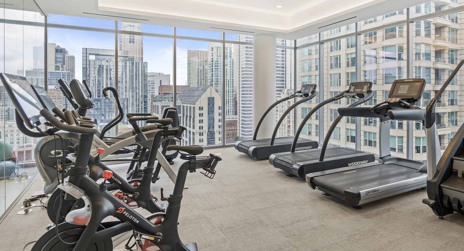 Modern cardio room with treadmills and exercise bikes, featuring large windows with city skyline views at Residences at 8 East Huron in Chicago