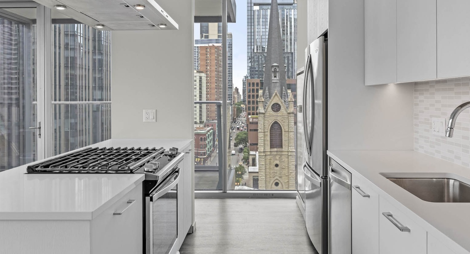 Contemporary kitchen featuring white cabinets, stainless steel appliances, and a unique view of a historic church at Residences at 8 East Huron in Chicago