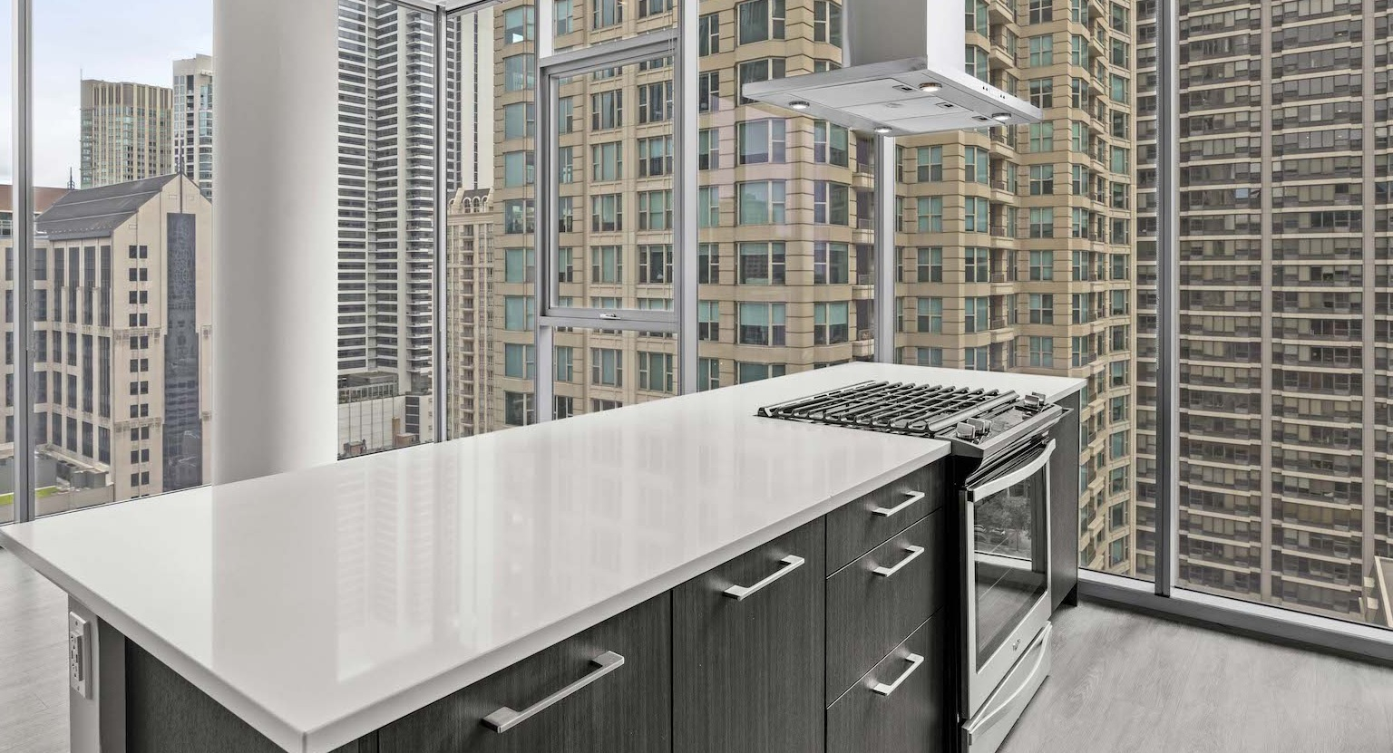 Sleek kitchen with a white island, contemporary appliances, and panoramic cityscape views through large windows at Residences at 8 East Huron in Chicago