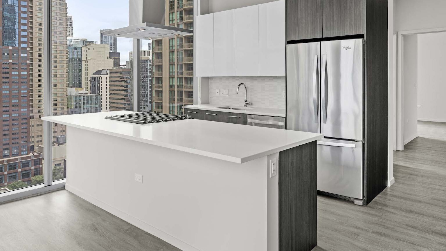 Modern kitchen with a large island, stainless steel appliances, and floor-to-ceiling windows offering city views at Residences at 8 East Huron in Chicago