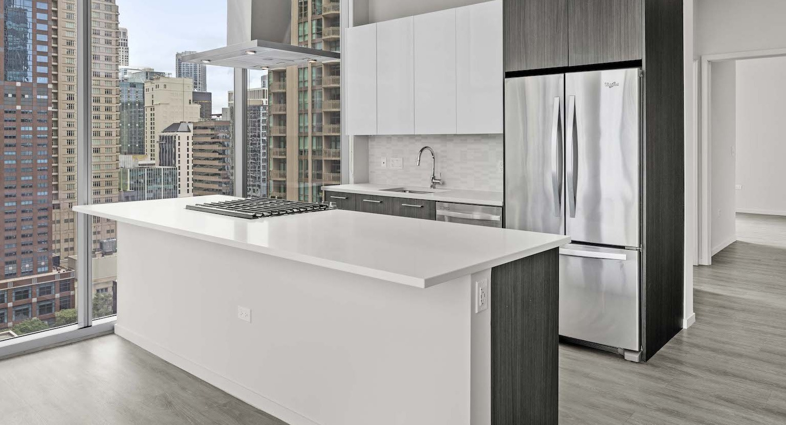 Modern kitchen with a large island, stainless steel appliances, and floor-to-ceiling windows offering city views at Residences at 8 East Huron in Chicago