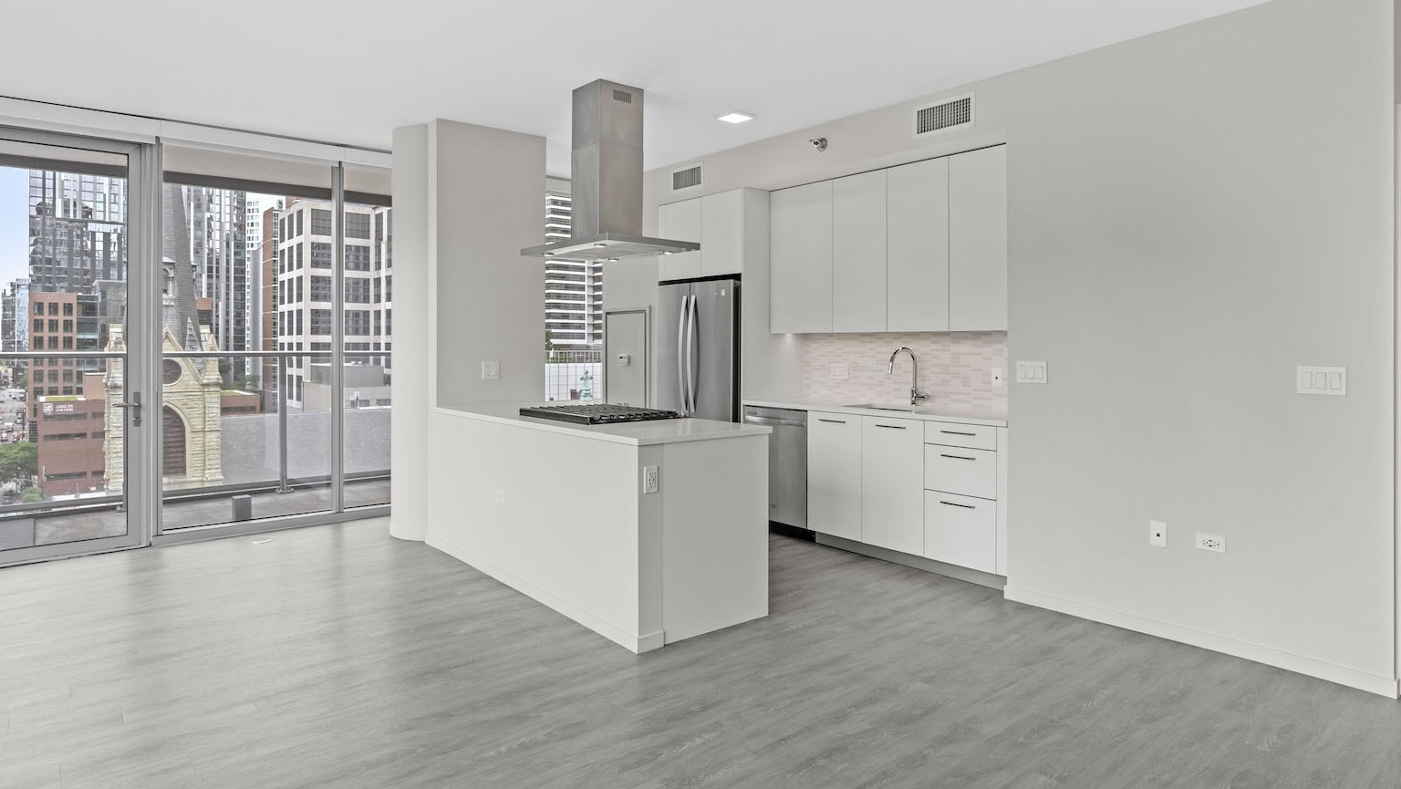 Bright, empty kitchen with an island, modern appliances, and an open layout flowing to a balcony with city views at Residences at 8 East Huron in Chicago