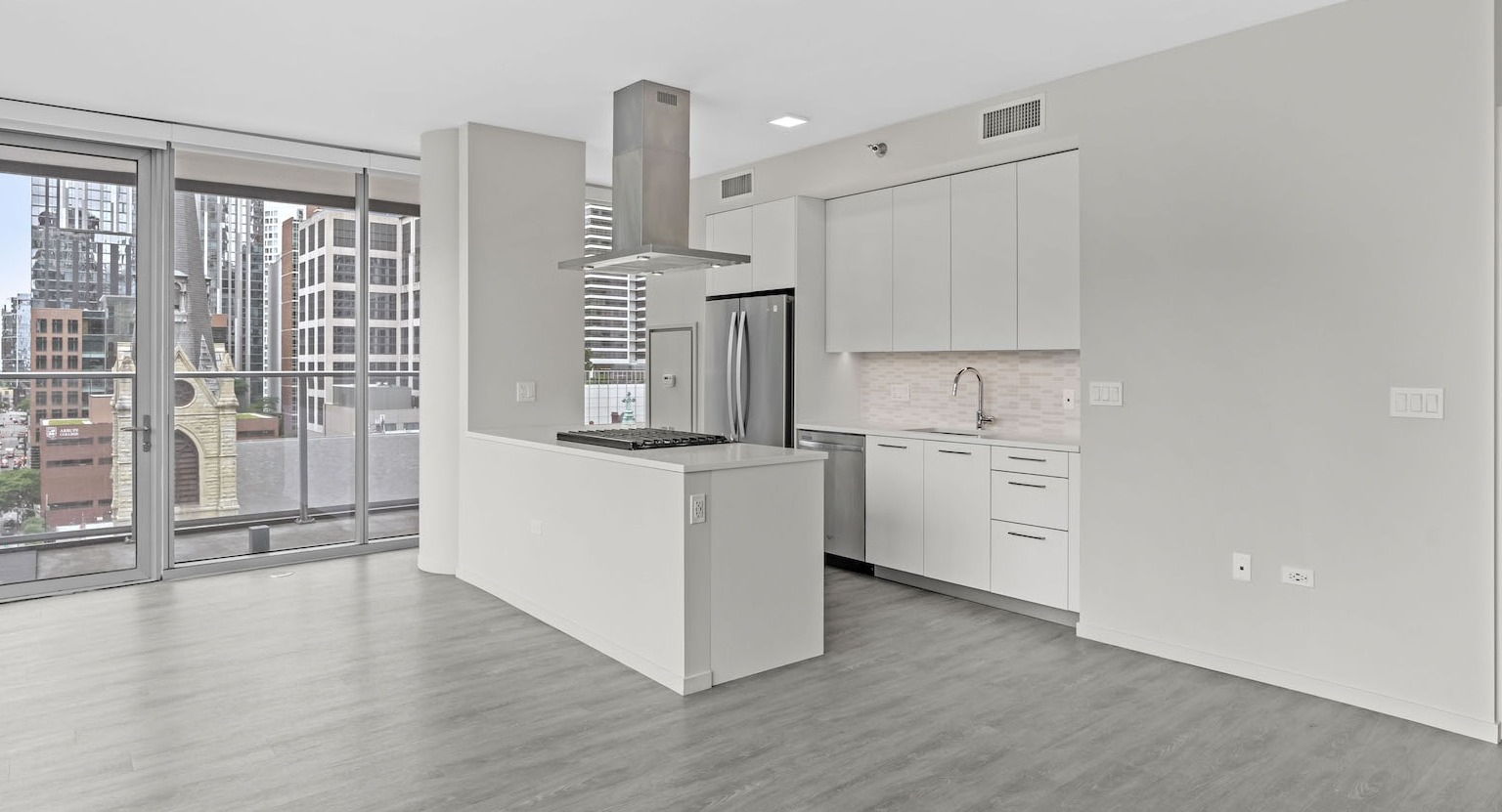 Bright, empty kitchen with an island, modern appliances, and an open layout flowing to a balcony with city views at Residences at 8 East Huron in Chicago