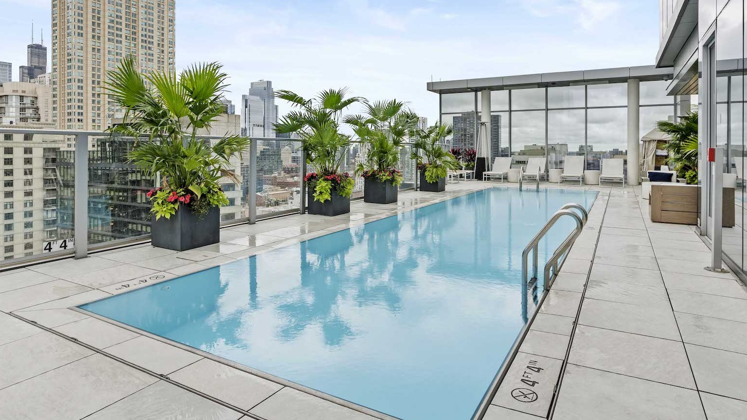 Stunning rooftop pool with lounge seating, lush planters, and impressive city views at Residences at 8 East Huron in Chicago