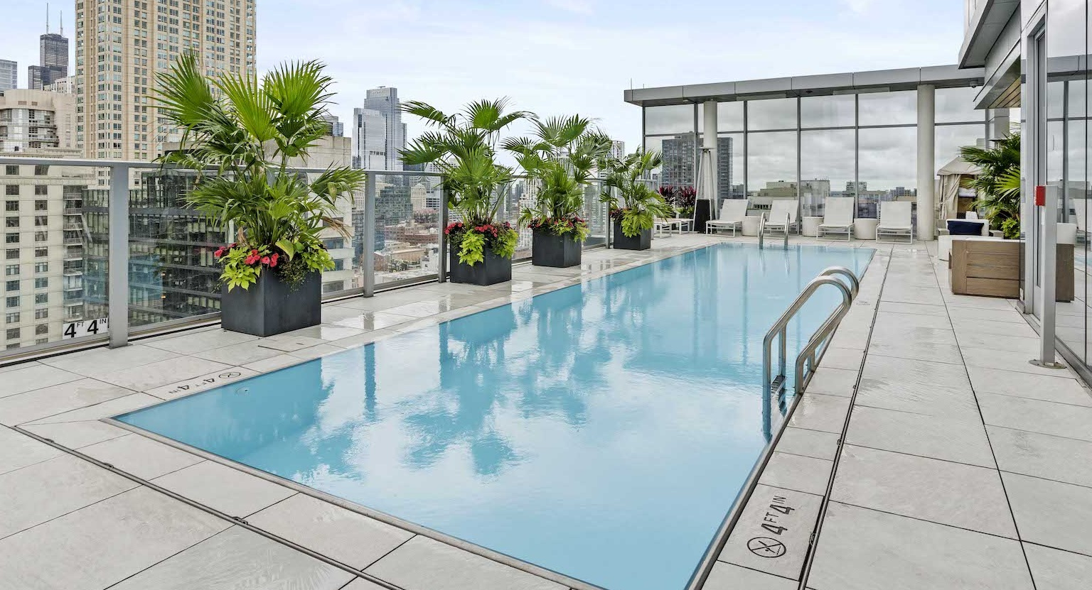 Stunning rooftop pool with lounge seating, lush planters, and impressive city views at Residences at 8 East Huron in Chicago