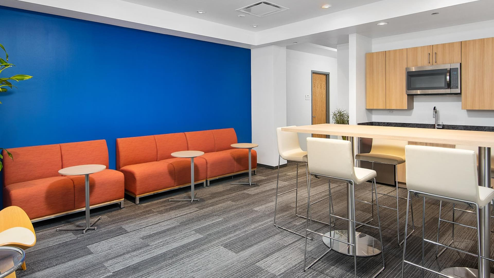 Resident kitchen lounge with high-top seating, orange sofas, and kitchenette against a bold blue wall at Optima Signature apartments in Chicago