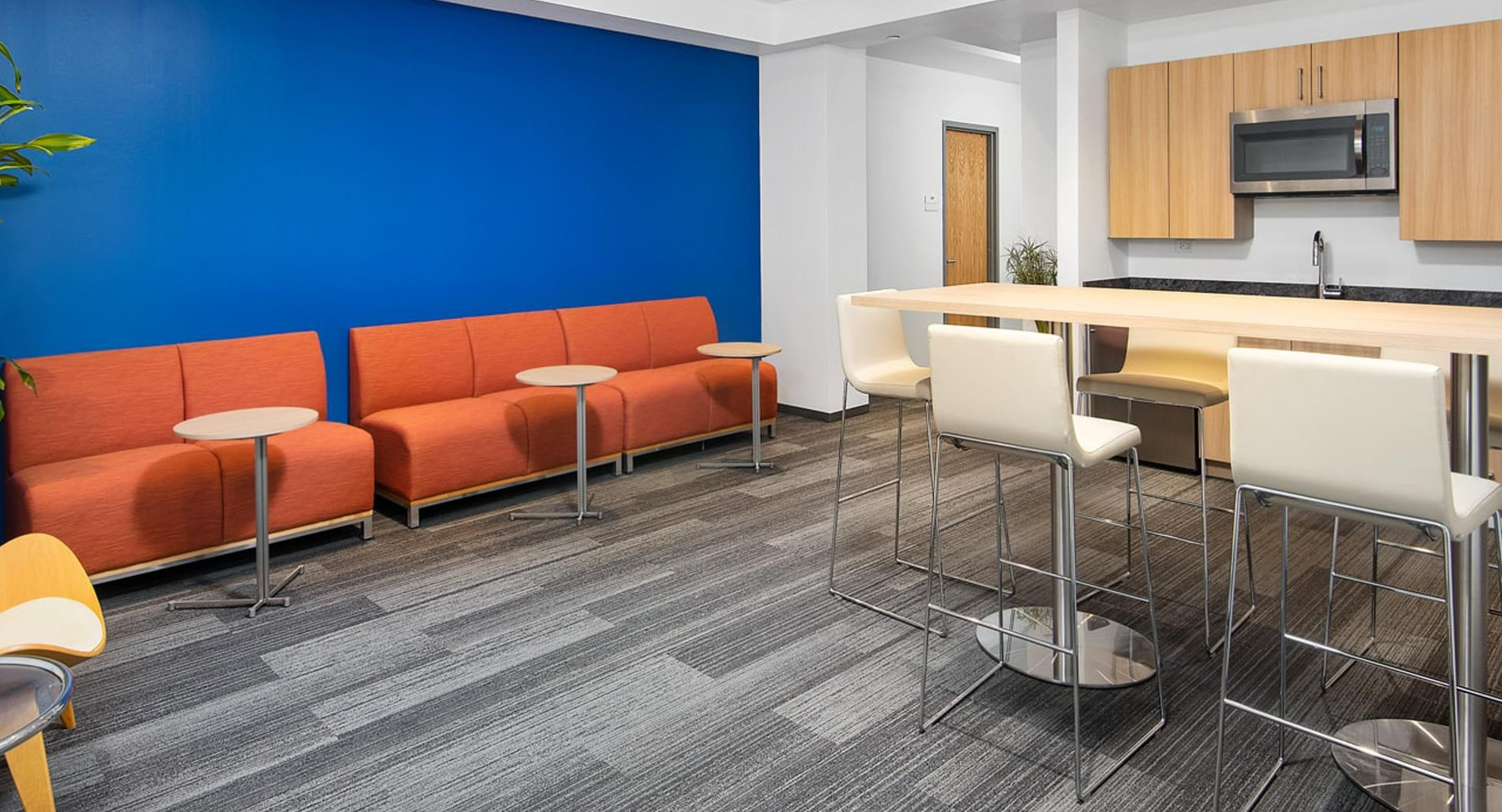 Resident kitchen lounge with high-top seating, orange sofas, and kitchenette against a bold blue wall at Optima Signature apartments in Chicago