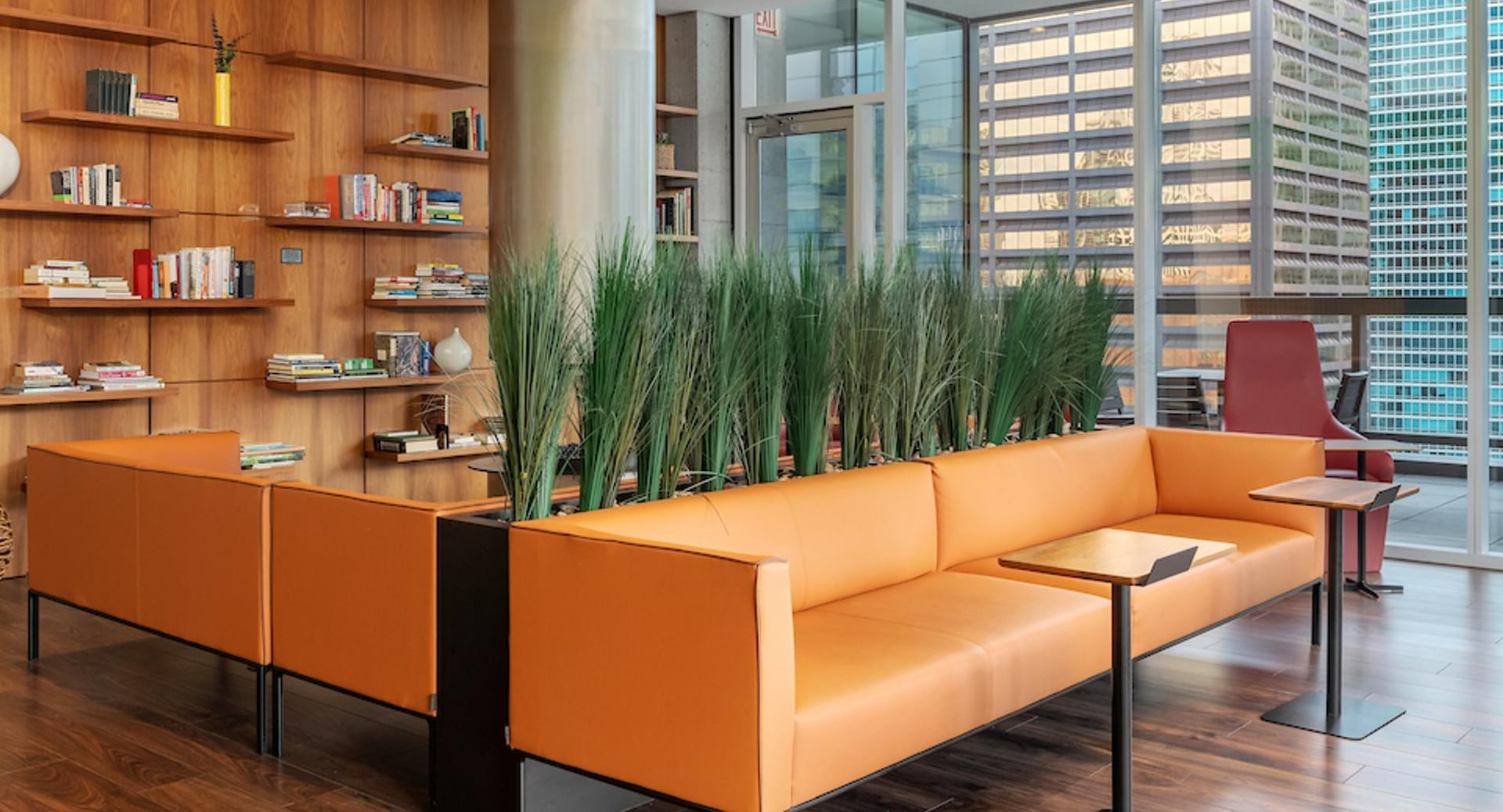 Resident lounge with orange leather sofas, indoor plants, and a central fireplace at Optima Signature apartments in downtown Chicago