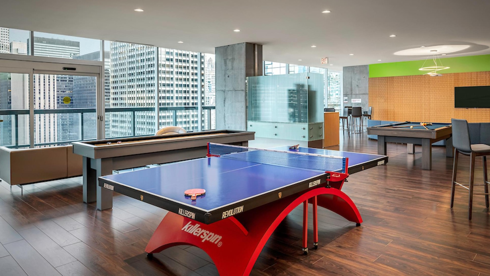 Spacious resident lounge with ping pong, pool tables, and floor-to-ceiling windows overlooking Chicago at Optima Signature apartments