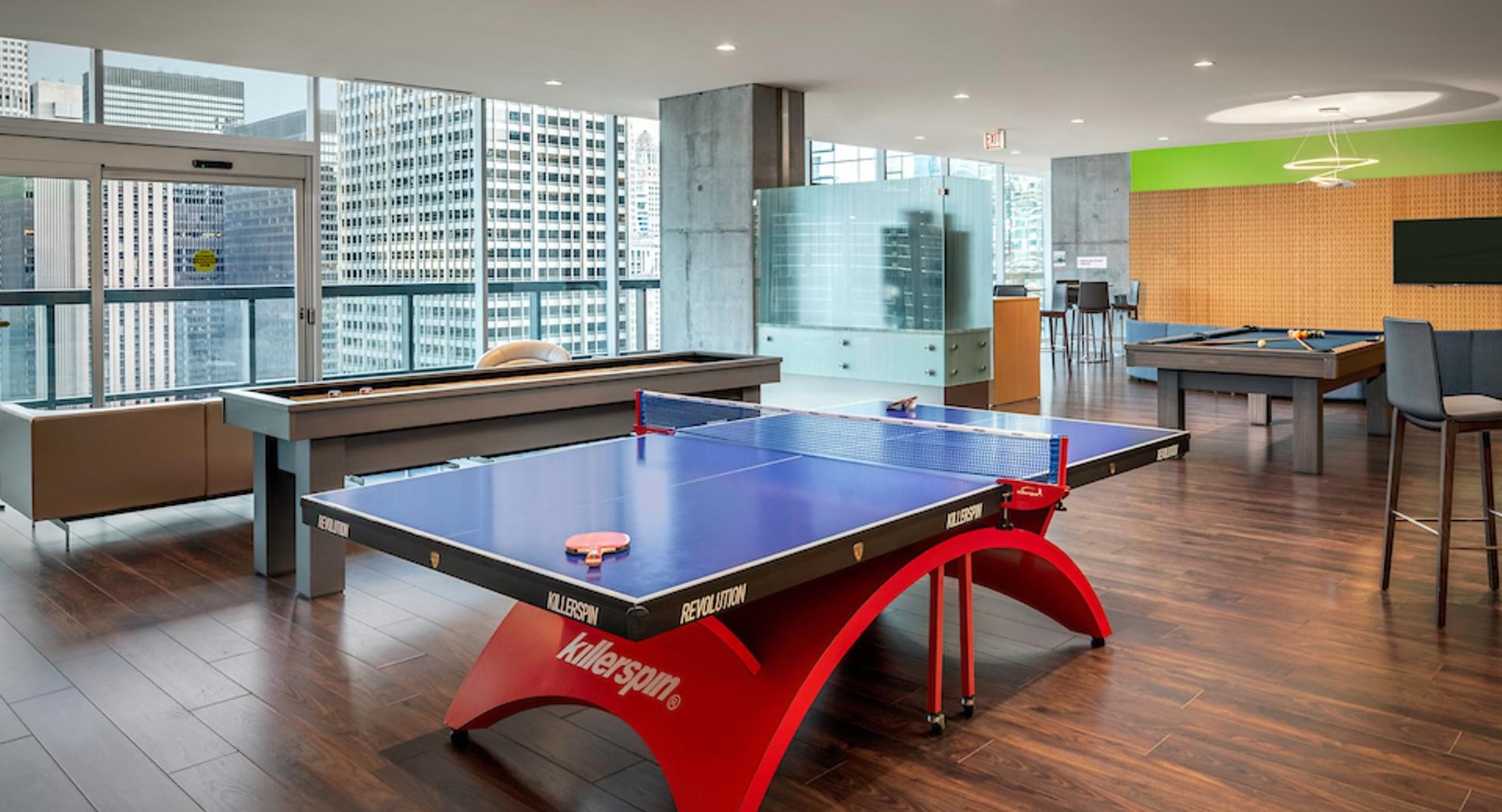 Spacious resident lounge with ping pong, pool tables, and floor-to-ceiling windows overlooking Chicago at Optima Signature apartments