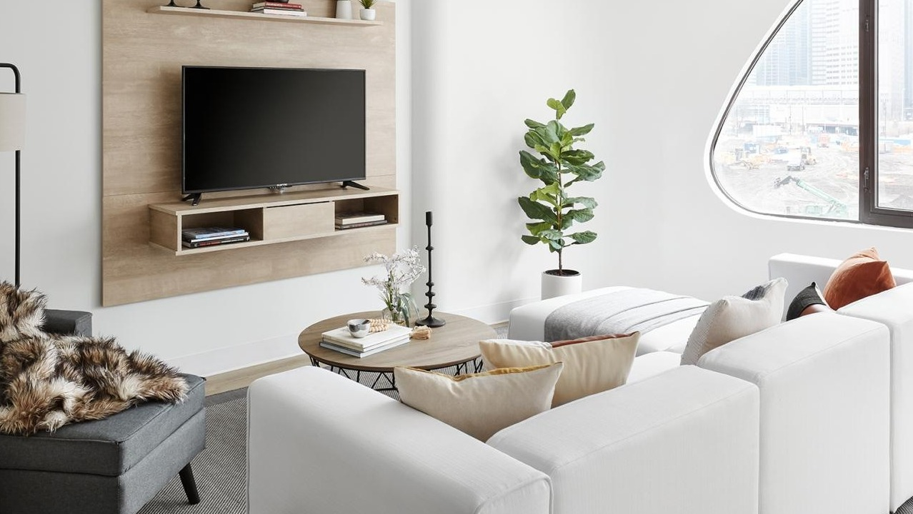 An inviting living room with a white sectional sofa, a grey armchair, a wall-mounted TV, and large windows at River City Apartments in Chicago