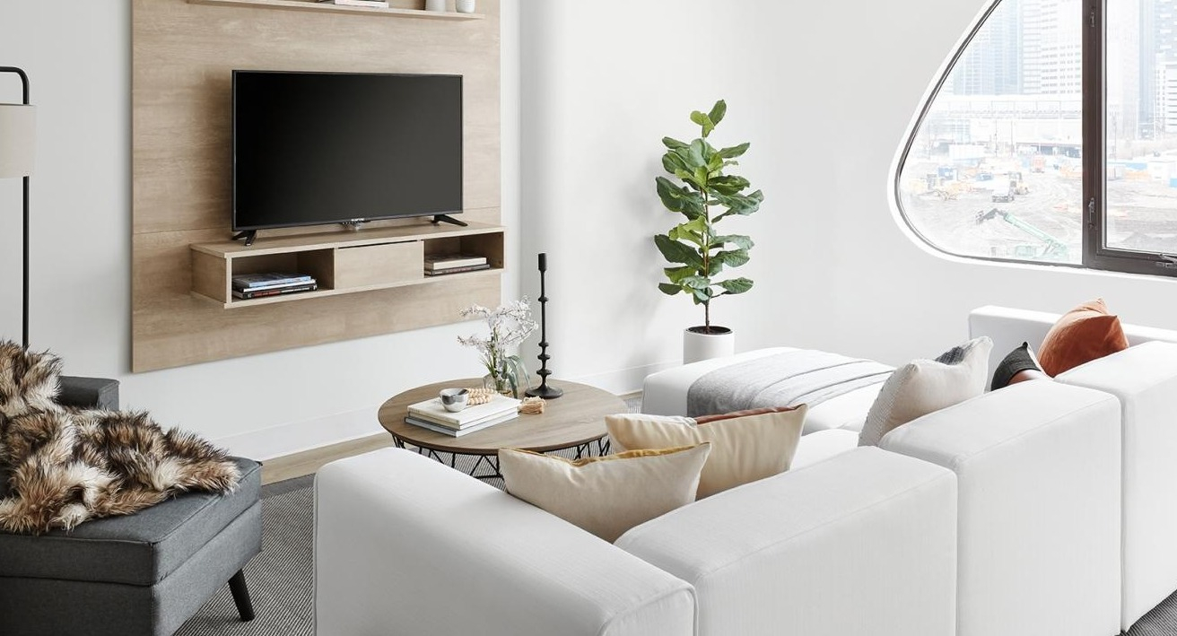 An inviting living room with a white sectional sofa, a grey armchair, a wall-mounted TV, and large windows at River City Apartments in Chicago