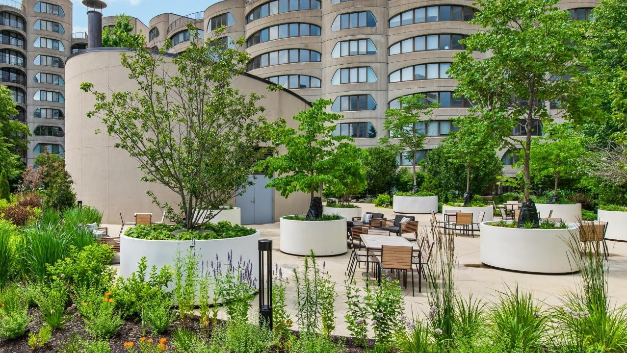 A lush outdoor courtyard with circular planters, various trees, and seating areas, surrounded by modern buildings at River City Apartments in Chicago