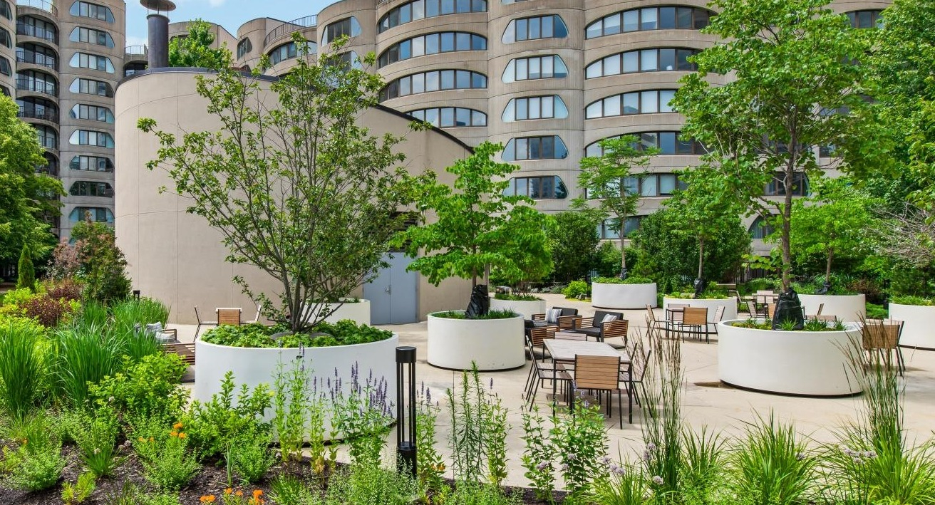 A lush outdoor courtyard with circular planters, various trees, and seating areas, surrounded by modern buildings at River City Apartments in Chicago