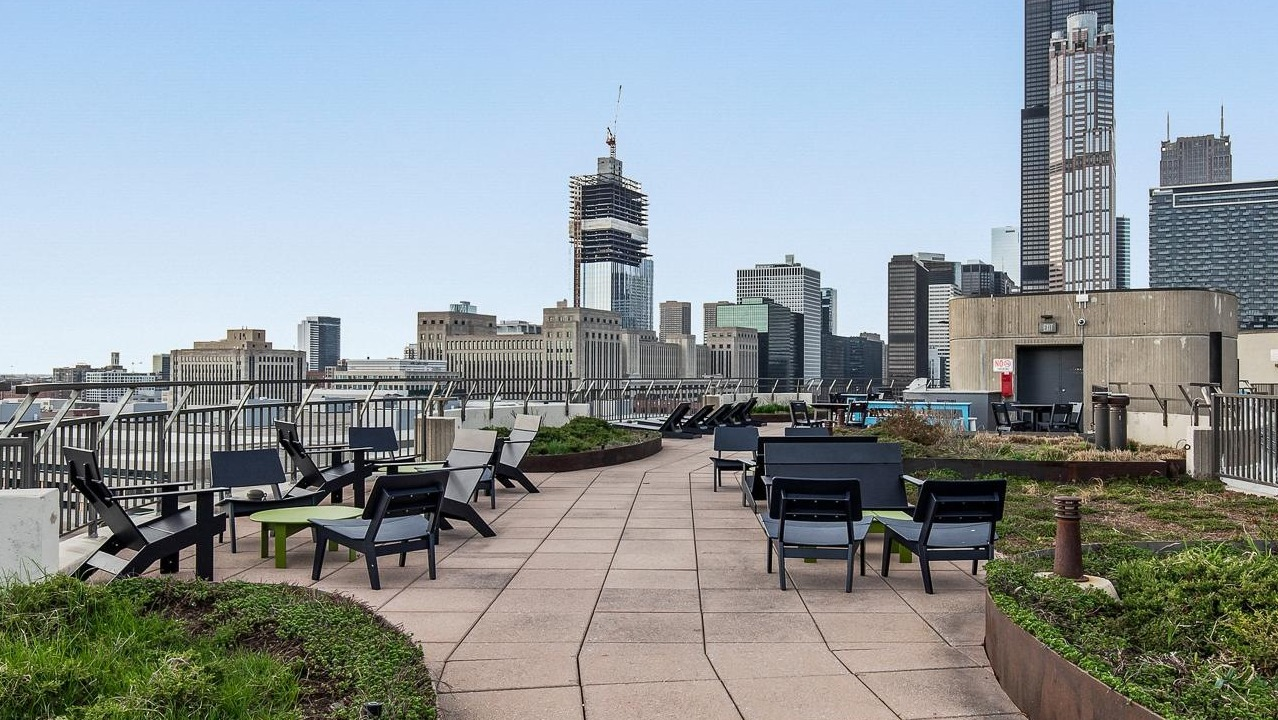 A rooftop lounge area with various seating, green landscaping, and a panoramic view of the Chicago city skyline at River City Apartments