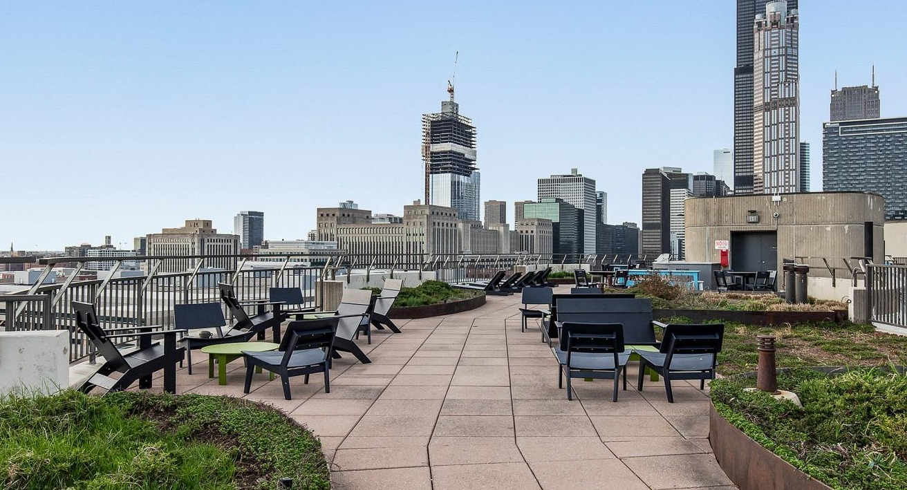 A rooftop lounge area with various seating, green landscaping, and a panoramic view of the Chicago city skyline at River City Apartments