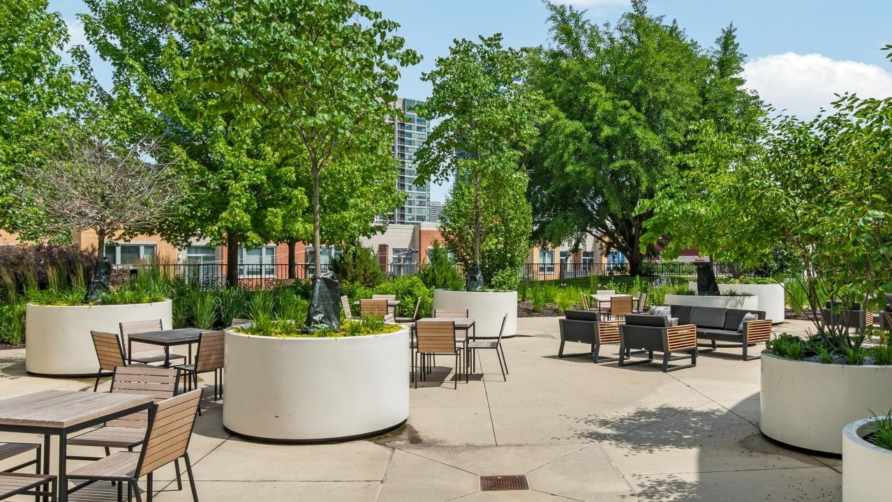 A spacious outdoor patio with multiple seating arrangements, mature trees in large planters, and a view of city buildings at River City Apartments in Chicago