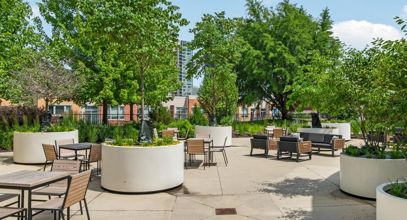 A spacious outdoor patio with multiple seating arrangements, mature trees in large planters, and a view of city buildings at River City Apartments in Chicago