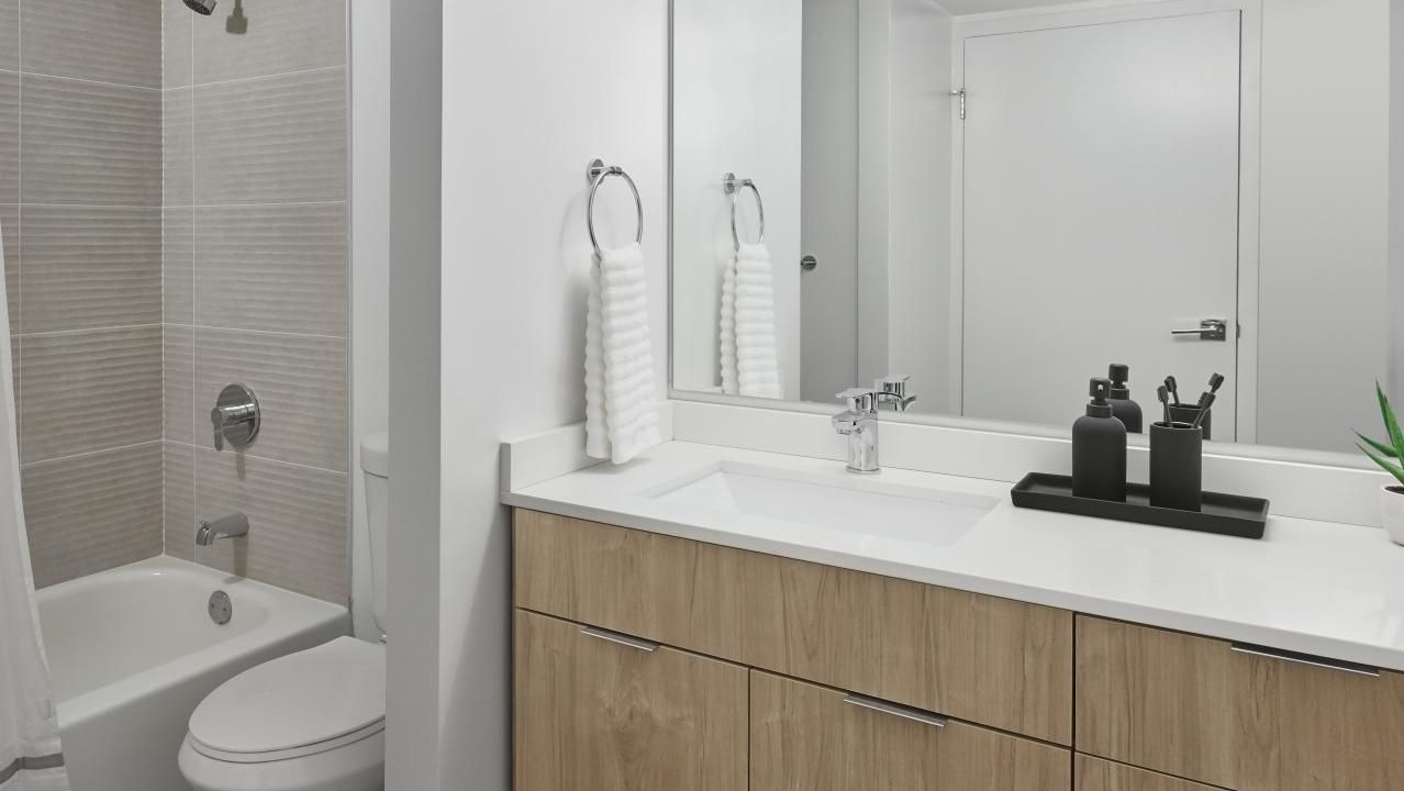 Modern bathroom with a wood vanity, white countertop, large mirror, and a clean tub and shower combo at River City Apartments in Chicago