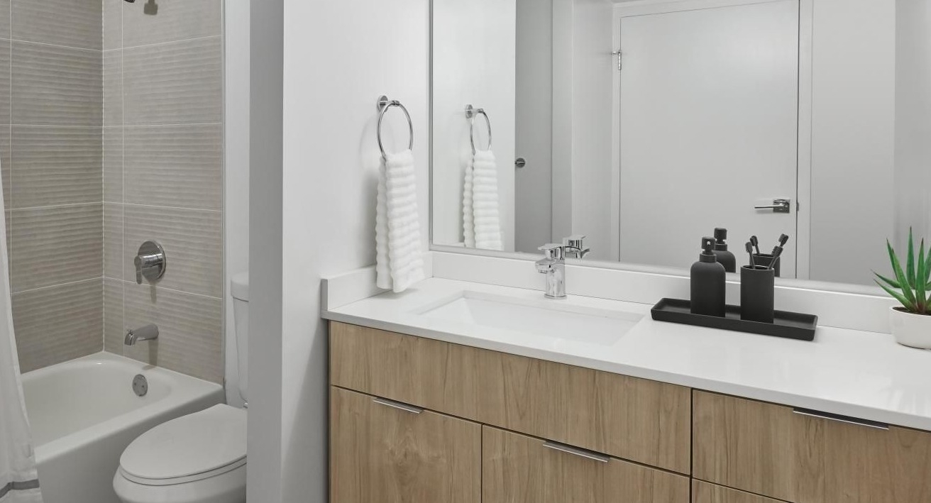 Modern bathroom with a wood vanity, white countertop, large mirror, and a clean tub and shower combo at River City Apartments in Chicago