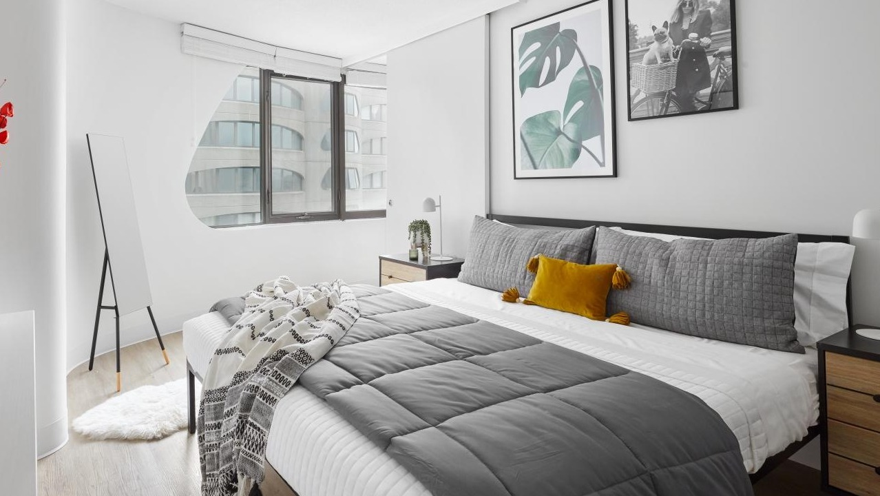 Chic and minimalist bedroom with a grey comforter, yellow accent pillow, and modern wall art at River City Apartments in Chicago