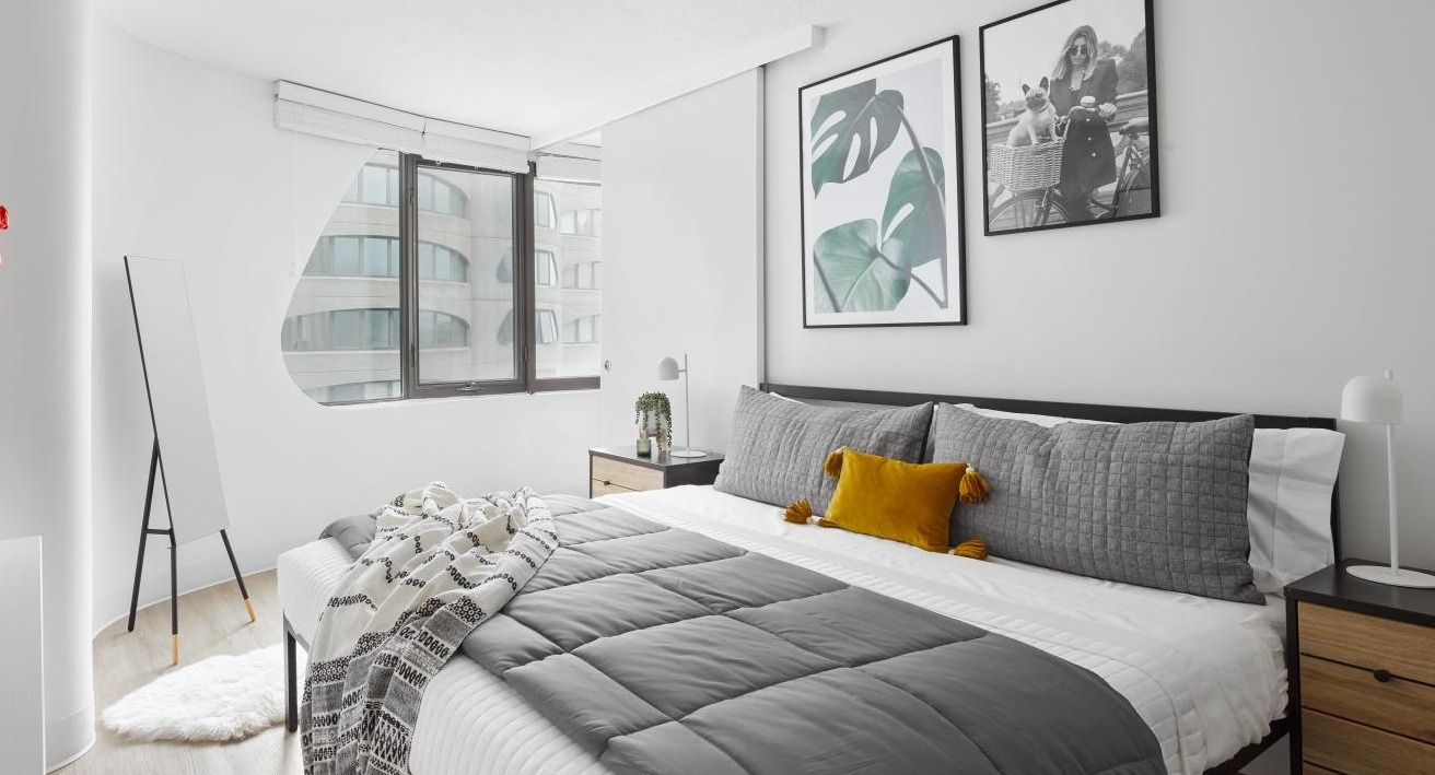 Chic and minimalist bedroom with a grey comforter, yellow accent pillow, and modern wall art at River City Apartments in Chicago