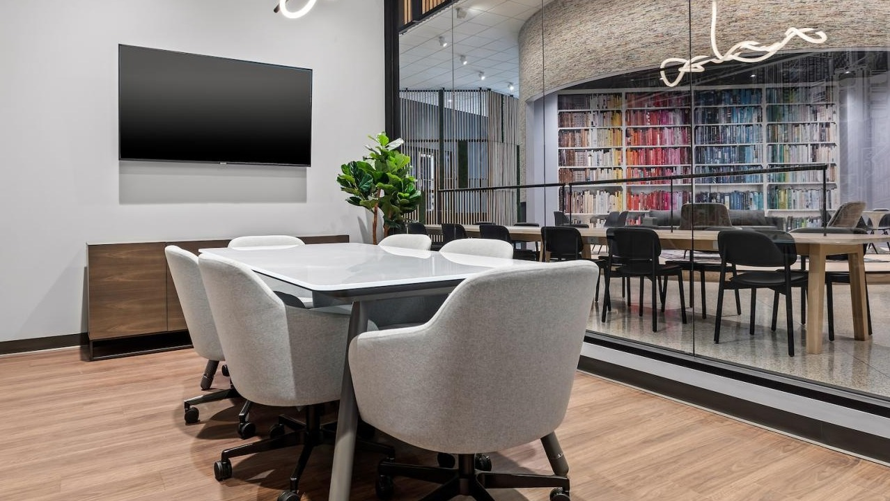 Modern conference room with a large table, comfortable chairs, and a glass wall overlooking a vibrant lounge at River City Apartments in Chicago