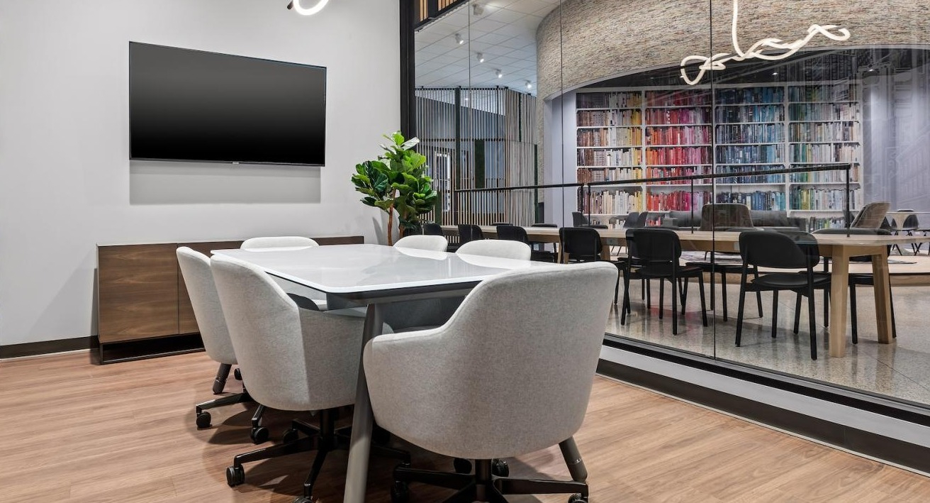 Modern conference room with a large table, comfortable chairs, and a glass wall overlooking a vibrant lounge at River City Apartments in Chicago