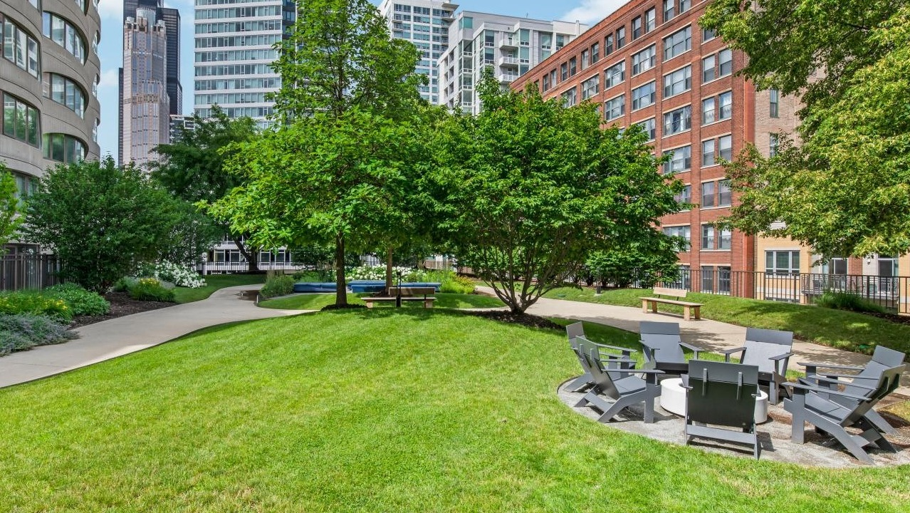 Lush green courtyard with a fire pit, seating, walking paths, and mature trees, offering a peaceful outdoor retreat at River City Apartments in Chicago
