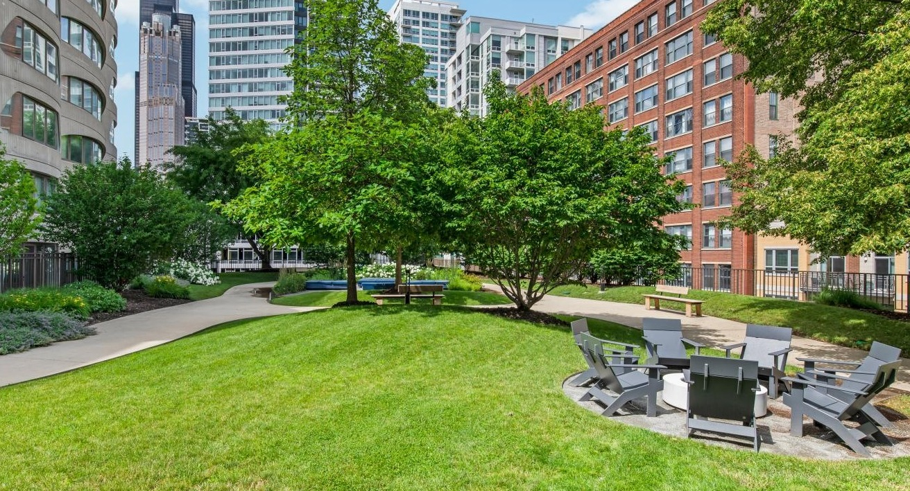 Lush green courtyard with a fire pit, seating, walking paths, and mature trees, offering a peaceful outdoor retreat at River City Apartments in Chicago