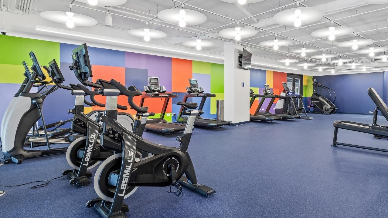 Energetic fitness center with cardio machines, weight equipment, and a colorful accent wall at River City Apartments in Chicago
