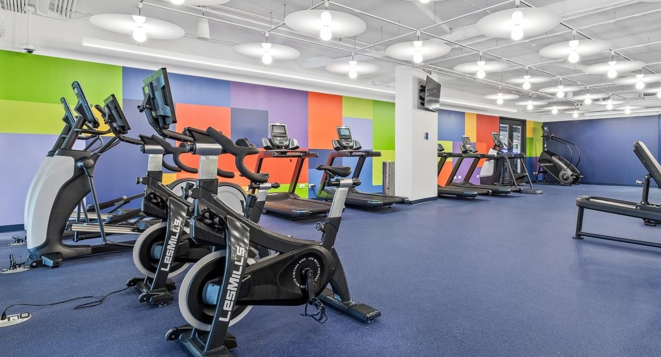 Energetic fitness center with cardio machines, weight equipment, and a colorful accent wall at River City Apartments in Chicago
